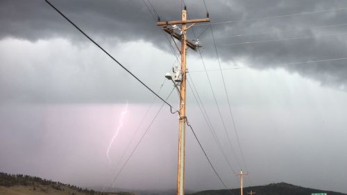 Low angle view of electricity pylon against storm clouds