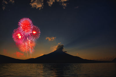 Firework display over lake against sky with mount fuji