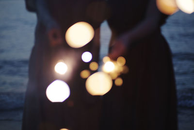 Midsection of women holding illuminated lights over sea