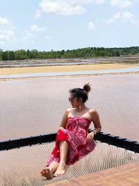 Woman sitting by lake against sky