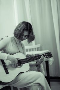 Young woman playing guitar while sitting at home