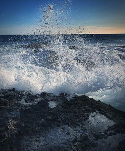 Sea waves splashing on shore against sky