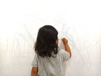 Picture from a back of a little girl drawing creatively on a white wall