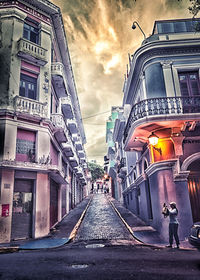 Road leading towards buildings against cloudy sky