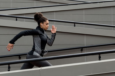 Side view of young woman running by wall