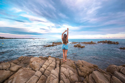 Rear view of person standing on rock by sea against sky