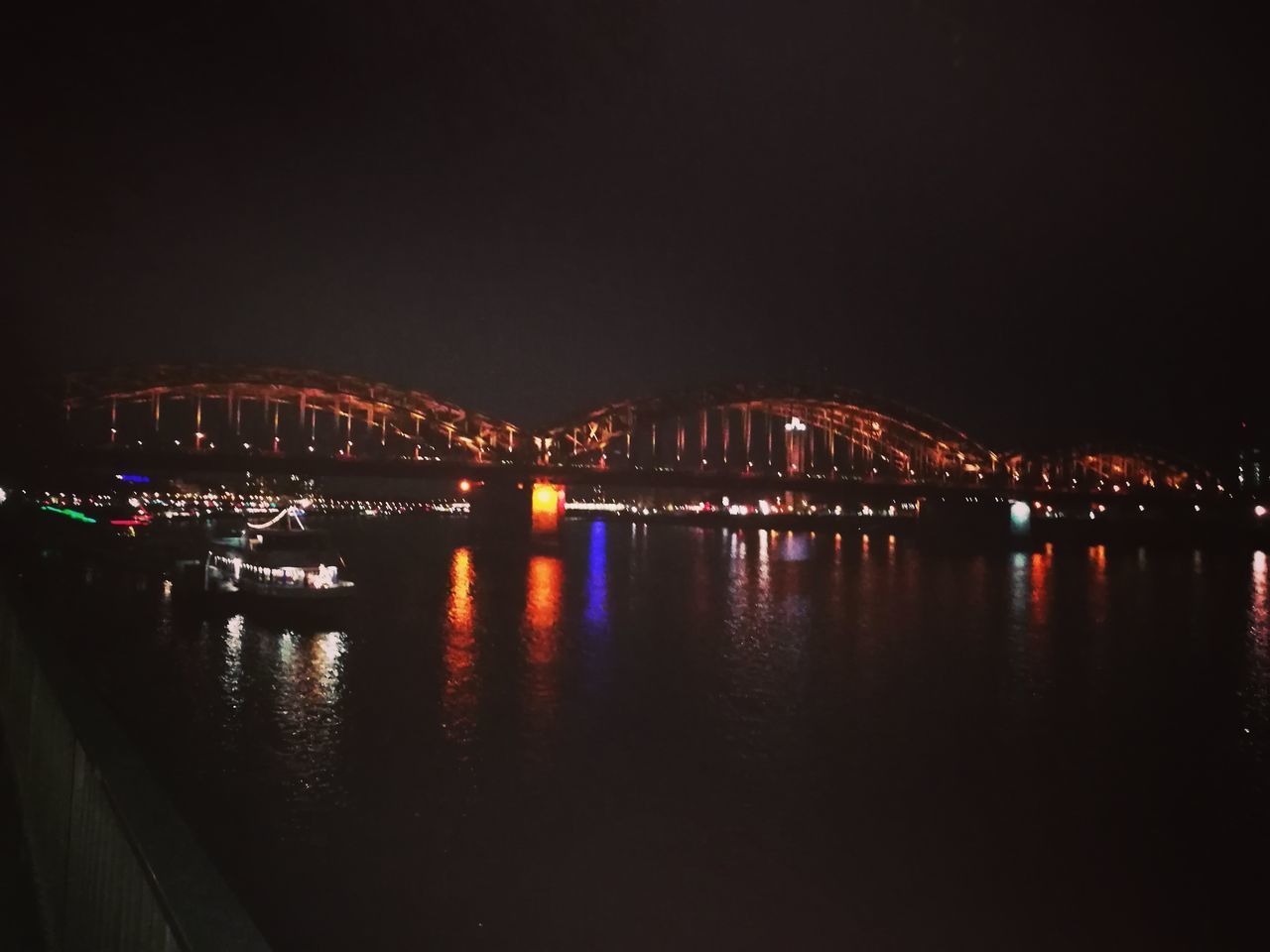 ILLUMINATED BRIDGE OVER RIVER AGAINST SKY AT NIGHT