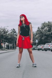 Full length of young woman with redhead standing on road against cloudy sky