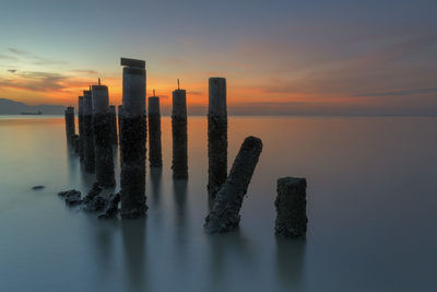 Wooden posts in sea against sky at sunset