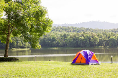 Tent on field by lake against sky