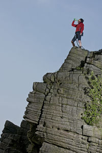 Low angle view of man standing on rock against sky