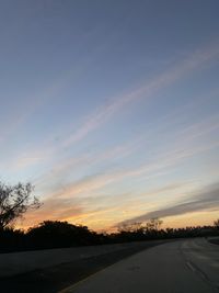 Road by silhouette trees against sky during sunset