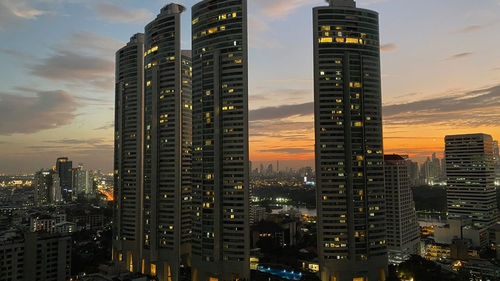 Illuminated buildings in city against sky at sunset