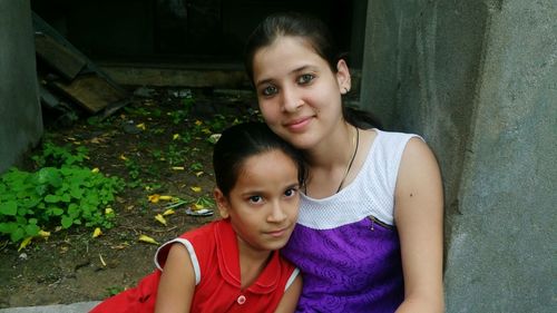 Portrait of mother and daughter sitting by wall