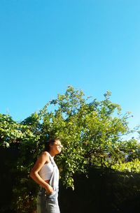 Woman standing by tree against clear blue sky