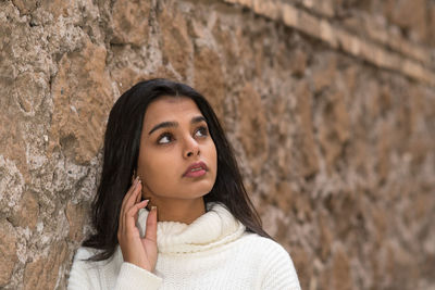 Portrait of a young woman looking away against wall