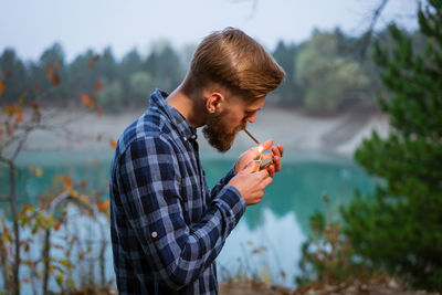 Smoking bearded man outdoors near lake in the evening. bad habit, addiction