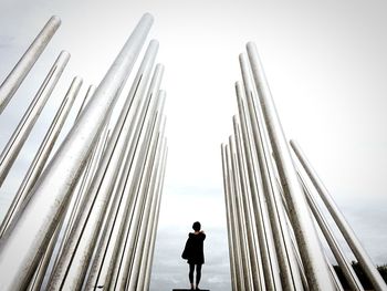 Rear view of woman standing amidst metal poles against sky