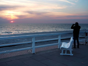 Rear view of man standing at beach during sunset