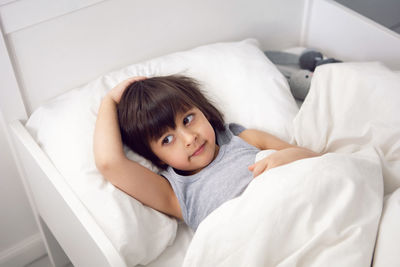 Child boy lies in a white children's bed with a blanket in a room with toys rabbits