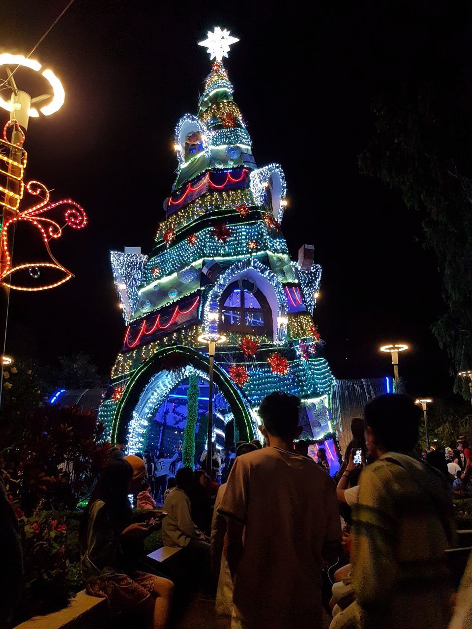 REAR VIEW OF PEOPLE AT ILLUMINATED CHRISTMAS TREE