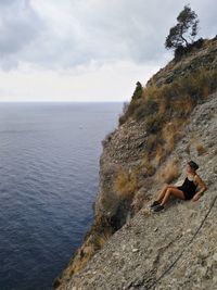 Man on rock by sea against sky