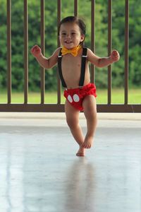 Playful shirtless baby boy wearing suspenders walking on floor