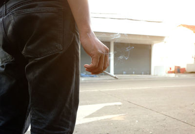 Midsection of man holding cigarette while standing on street