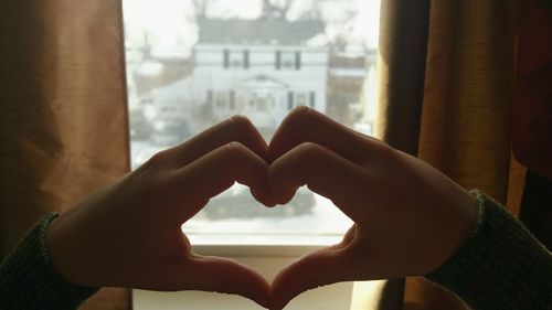 Cropped hands making heart shape against window