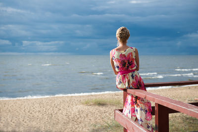 Rear view of woman sitting on railing against beach