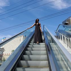 Low angle view of woman standing on escalator against sky