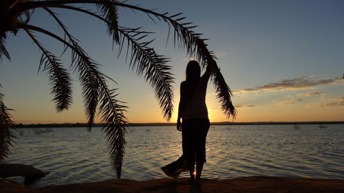 Silhouette person standing by swimming pool against sea during sunset