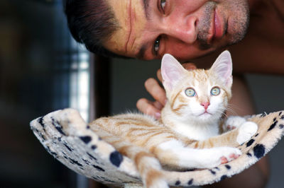 Portrait of man stroking kitten sitting on scratching post