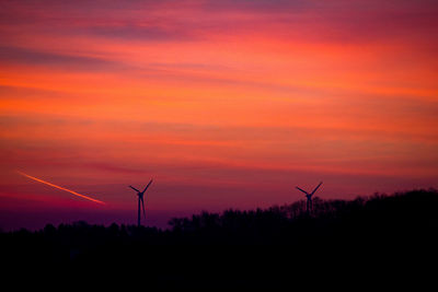 Silhouette windmills on field against orange sky