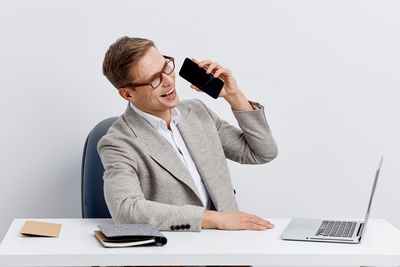 Young man using mobile phone while standing against white background