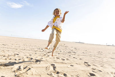 Playful boy jumping at beach on sunny day