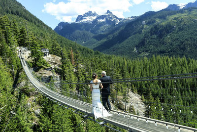 Couple walking on rope bridge against mountain range