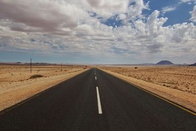 Empty country road against cloudy sky