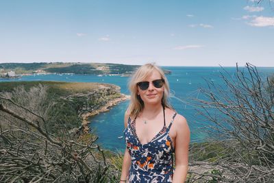 Young woman wearing sunglasses standing at beach against sky
