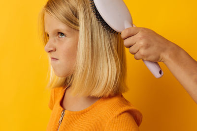 Cropped hand combing hair of girl against colored background