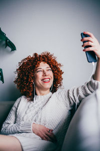 Smiling woman taking selfie while sitting on sofa at home
