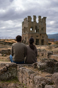 Rear view of men sitting on stone wall