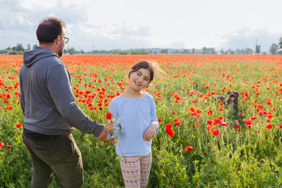 Father and daughter standing in the poppy field next to their running dog