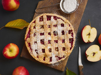 Baked round traditional apple pie on brown wooden board and fresh red apples, top view