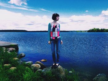 Full length of girl standing on rock against lake and cloudy sky