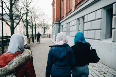 Rear view of females walking on footpath by building in city