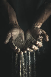 Cropped hands of man holding sand against black background