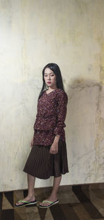 Portrait of a young woman standing against wall