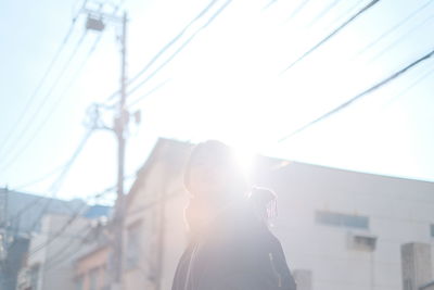 Woman standing in city against bright sky