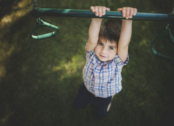 High angle portrait of boy hanging on monkey bars in playground